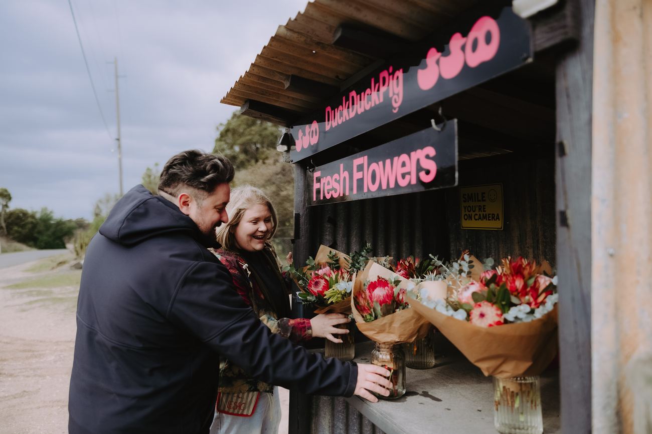 Two visitors choosing wrapped protea bunches at the Duck Duck Pig roadside flower stall